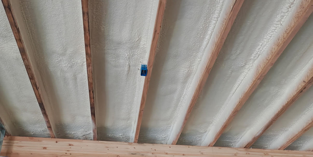 Close-up image of spray-applied closed-cell foam insulation filling wall cavities between wooden studs in a residential construction project.