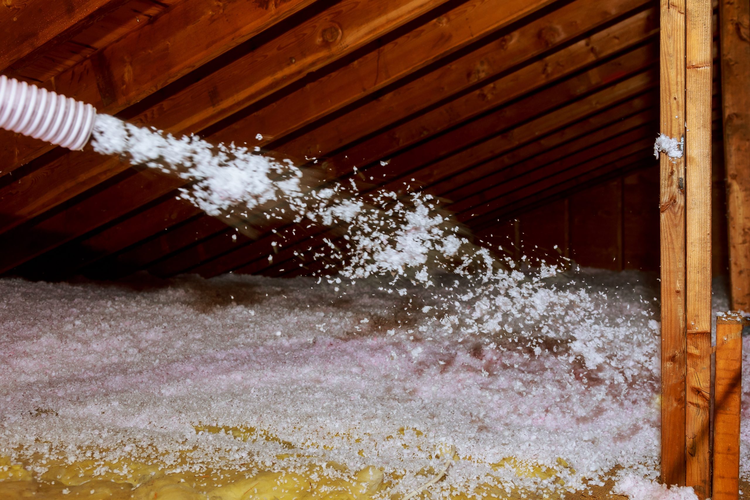 Technician using a hose to install blown-in insulation in an attic to improve energy efficiency.