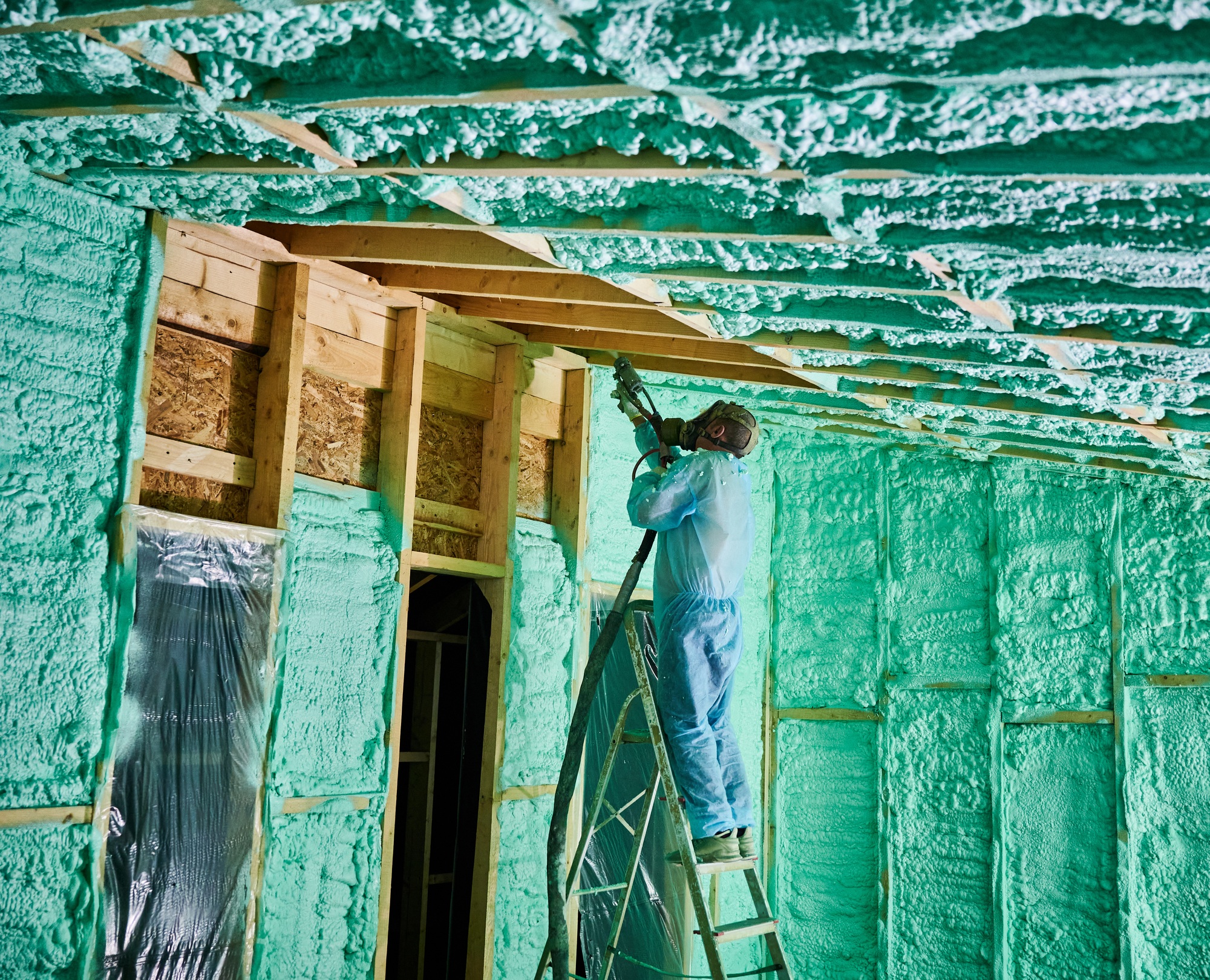 Worker spraying polyurethane foam for insulating wooden frame house. open cell