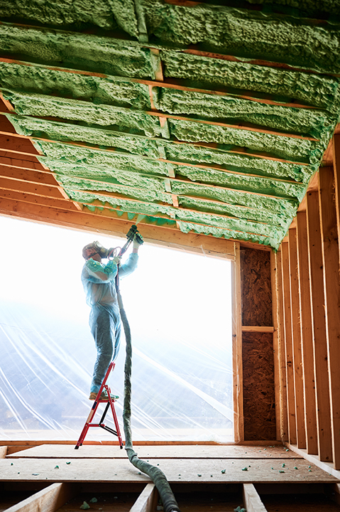 Insulation King worker spraying polyurethane foam for insulating wooden frame house.